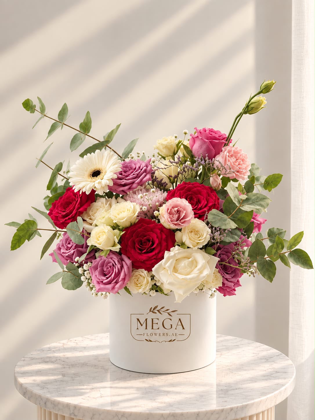 MÉGA branded ivory flower box with red, pink and cream roses, gerbera and eucalyptus in natural sunlight